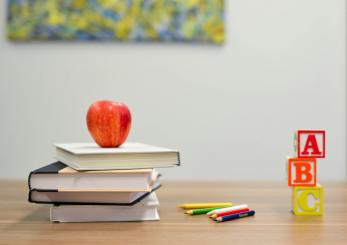 stack of books holding up an apple, colored pencils, and alphabet blocks on a desk